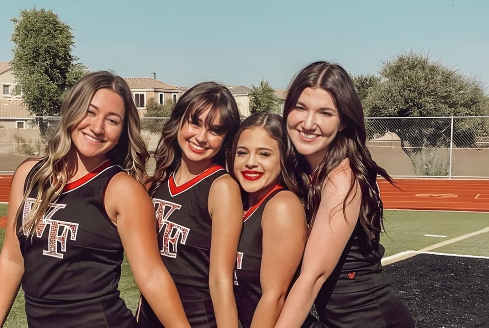 Vier Schülerinnen der Williams Field High School posieren gemeinsam auf dem Sportfeld vor Gebäuden und Bäumen.