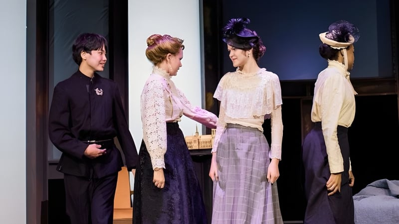 Vier Schüler der Williston Northampton School stehen in aufwendigen Kostümen und Frisuren auf einer Bühne vor dunklem Hintergrund.