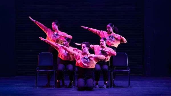 Eine Gruppe von Schülerinnen und Schülern der Williston Northampton School führt auf einer dunklen Bühne in farbenfrohen Kostümen eine Tanzaufführung auf.