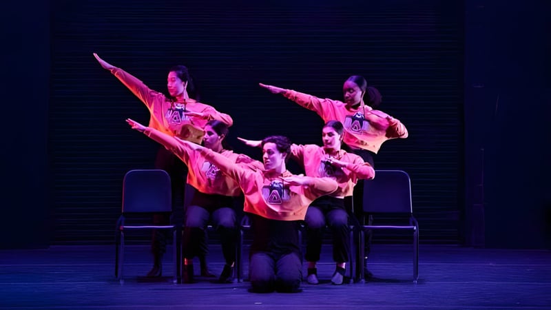 Eine Gruppe von Schülerinnen und Schülern der Williston Northampton School führt auf einer dunklen Bühne in farbenfrohen Kostümen eine Tanzaufführung auf.