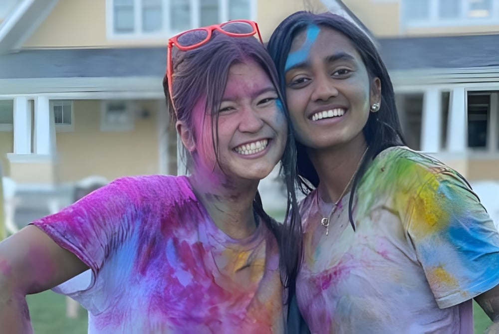 Zwei Schülerinnen der The Williston Northampton School stehen lachend vor einem Gebäude mit festlicher Atmosphäre.