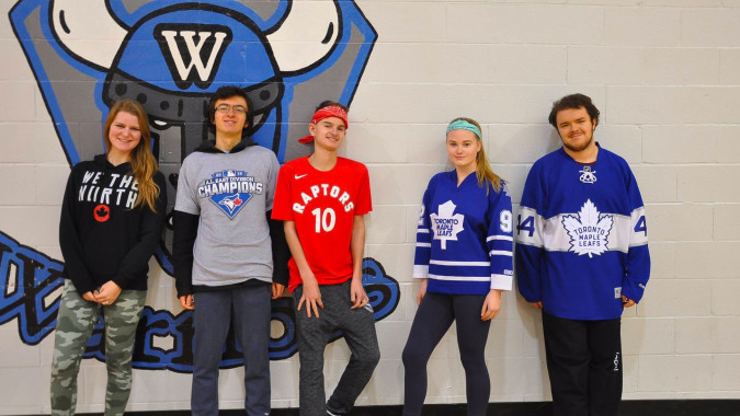 Fünf Personen stehen vor einem großen Sport-Wandbild auf dem Campus der WillowWood School.