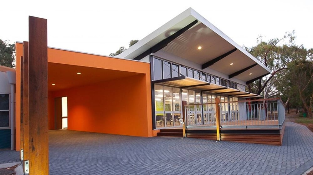 Das moderne, kantige Gebäude der Willunga High School mit oranger Außenfassade steht von Bäumen umgeben an einem gepflasterten Weg.