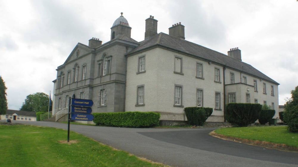 Das mehrstöckige Steingebäude der Wilson's Hospital School steht auf einer Rasenfläche umgeben von Bäumen und einem gepflasterten Zufahrtsweg.