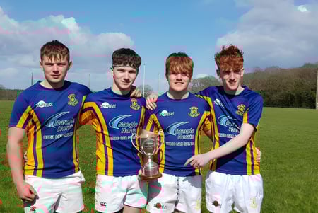 Vier Schüler der Wilson's Hospital School stehen auf einem Rasenfeld und halten gemeinsam eine Sporttrophäe.