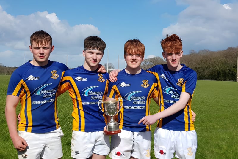 Vier Schüler der Wilson's Hospital School stehen auf einem Rasenfeld und halten gemeinsam eine Sporttrophäe.