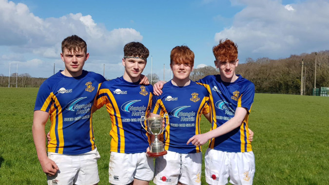 Vier Schüler der Wilson's Hospital School stehen auf einem Spielfeld und halten gemeinsam einen Pokal.