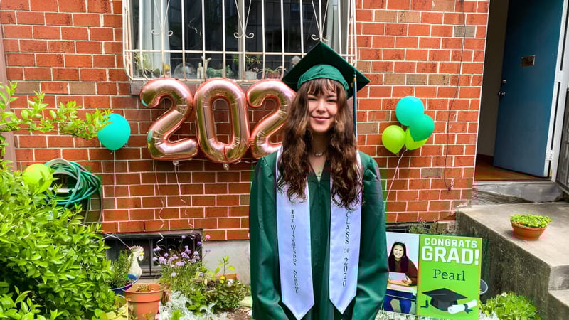 Eine junge Frau in grünem Abschlussmantel steht vor einer Backsteinwand mit Ballons, die 2022 formen, auf dem Campus der Winchendon School in New York City.