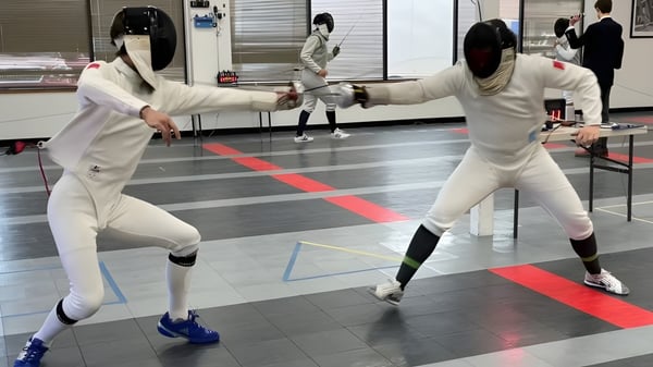 Zwei Schülerinnen und Schüler tragen Fechtkleidung und führen ein Duell im Fechtsport auf dem Gelände des Winchester College durch.