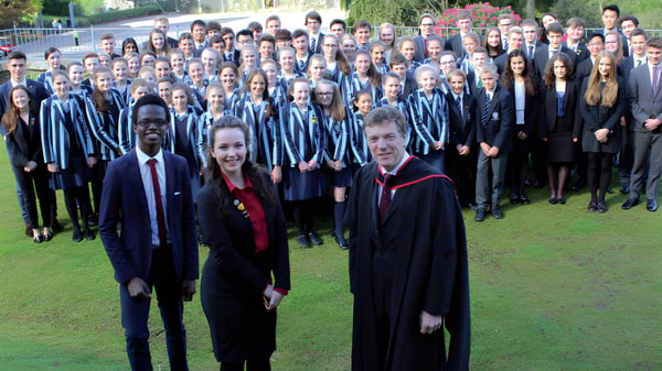 Eine Gruppe von Schülerinnen und Schülern der Windermere School steht in Abschlussroben auf einer Wiese vor einem Gebäude.
