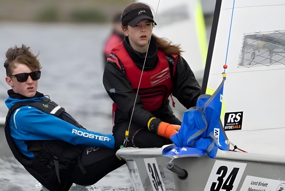 Zwei Personen stehen neben einem Fahrzeug mit dem Rooster-Logo auf dem Gelände der Windermere School.