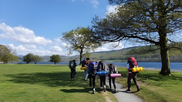 Schüler der Windermere School gehen auf einer Wiese nahe einem Gewässer mit Bäumen und blauem Himmel.