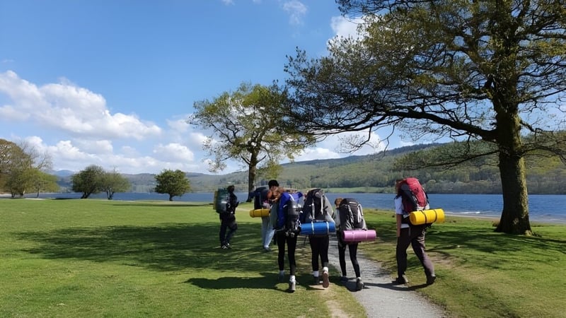 Schüler der Windermere School gehen auf einer Wiese nahe einem Gewässer mit Bäumen und blauem Himmel.
