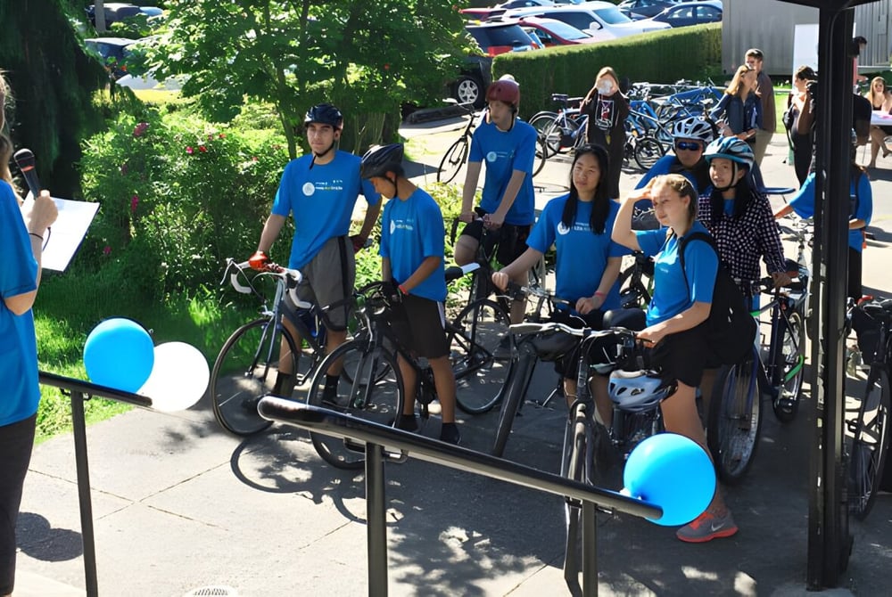Eine Gruppe von Schülerinnen und Schülern der Windermere Secondary School steht mit Fahrrädern vor einem bewaldeten Hintergrund.