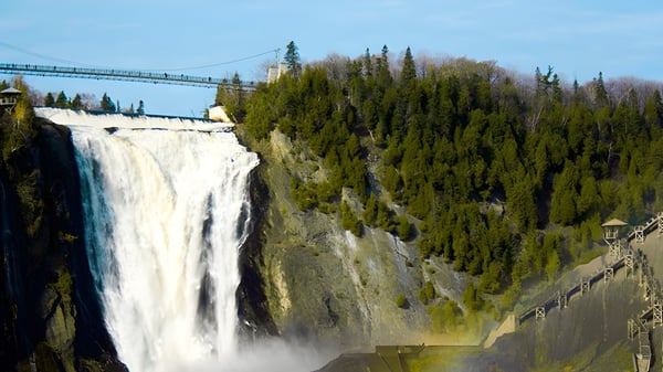 Ein Wasserfall fällt über einen felsigen Abhang vor einem Wald und einer Hängebrücke auf dem Campus der Windermere Secondary School.