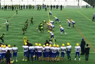 Eine Gruppe von Fußballspielern steht auf dem Spielfeld der Windsor Secondary School mit Zuschauern und Trainern im Hintergrund.