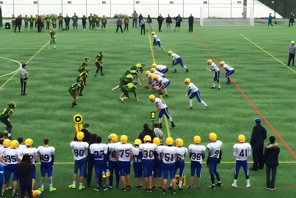 Eine Gruppe von Fußballspielern steht auf dem Spielfeld der Windsor Secondary School mit Zuschauern und Trainern im Hintergrund.