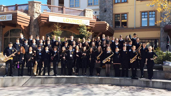 Eine große Gruppe von Menschen in formeller Kleidung versammelt sich im Außenbereich der Windsor Secondary School vor Holzbauten.