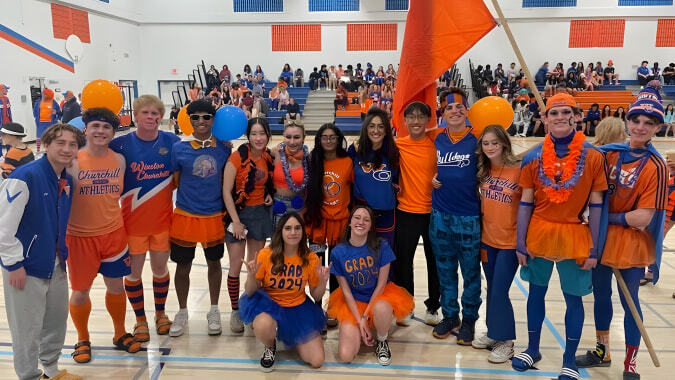Schüler der Winston Churchill High School versammeln sich in der Sporthalle mit Fahnen und Bannern im Hintergrund.