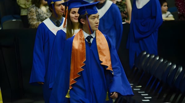 Eine Gruppe von Absolventen in blauen und orangenen Talaren steht bei einer Abschlussfeier der Winston Churchill High School.