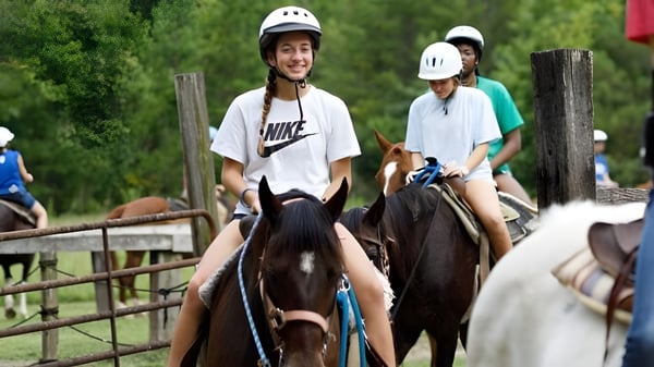 Zwei Personen reiten mit Helmen auf Pferden in einem umzäunten Außenbereich auf dem Campus der Winston Salem Christian School.