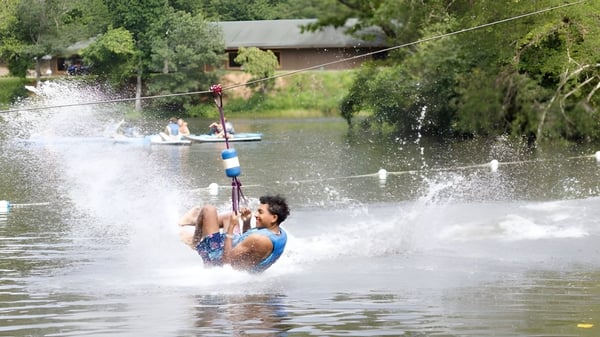 Eine Schülerin oder ein Schüler der Winston Salem Christian School fährt auf einem Wakeboard hinter einem Boot auf dem Wasser.