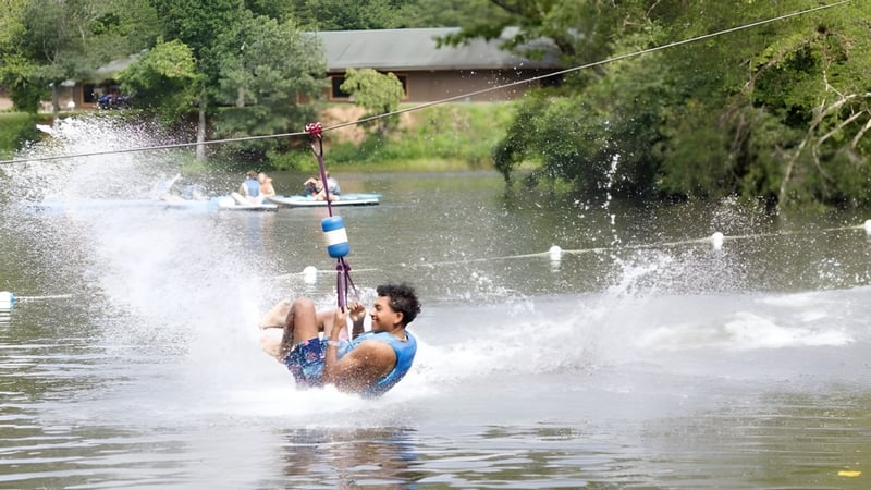 Eine Schülerin oder ein Schüler der Winston Salem Christian School fährt auf einem Wakeboard hinter einem Boot auf dem Wasser.