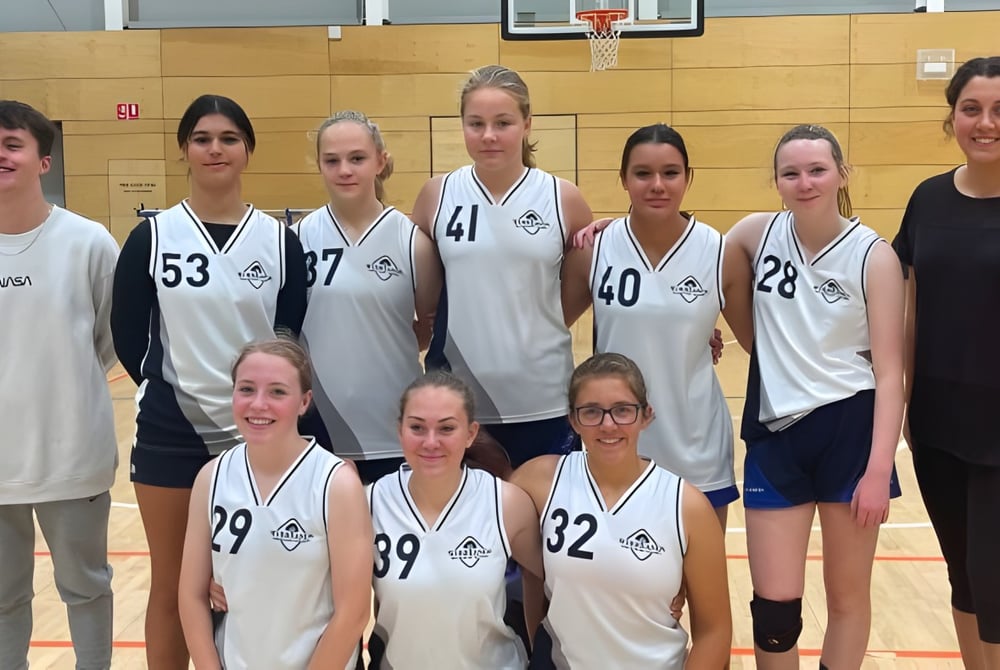 Eine Gruppe junger Basketballspielerinnen posiert gemeinsam in der Sporthalle der Wirreanda Secondary School vor einem Basketballkorb.
