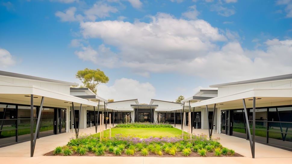 Das moderne Gebäude der Wirreanda Secondary School ist von einem gepflegten Garten umgeben und unter einem blauen Himmel mit Wolken zu sehen.