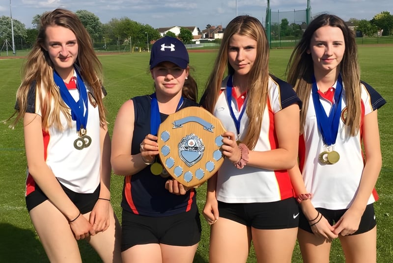 Vier Schülerinnen der Wisbech Grammar School halten auf dem Sportplatz Medaillen und einen Pokal.