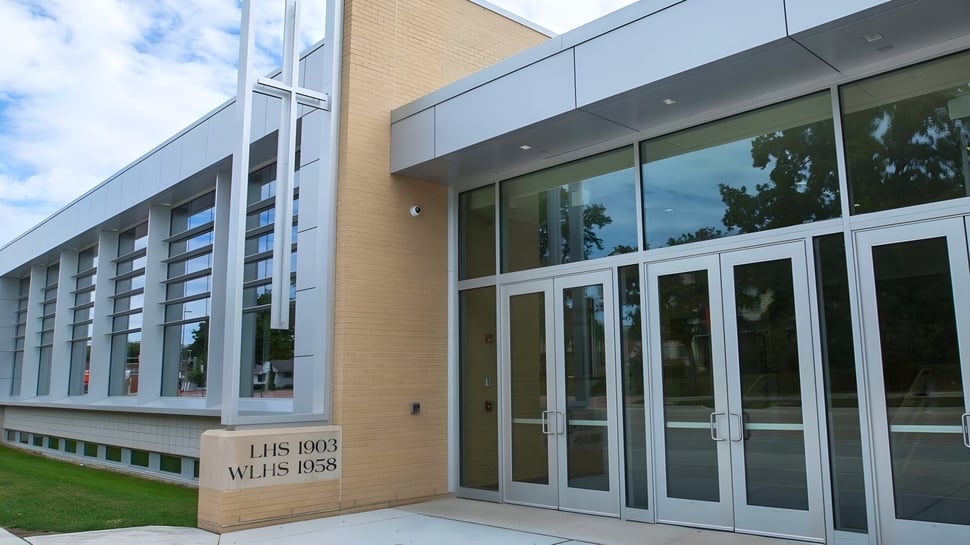 Das moderne Gebäude der Wisconsin Lutheran High School mit Glasfront und Backsteinfassade ist von einer grünen Fläche und Bäumen umgeben.