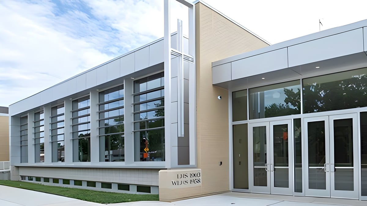 Das moderne mehrstöckige Gebäude mit großen Glasfenstern der Wisconsin Lutheran High School ist umgeben von Grünflächen unter bewölktem Himmel.