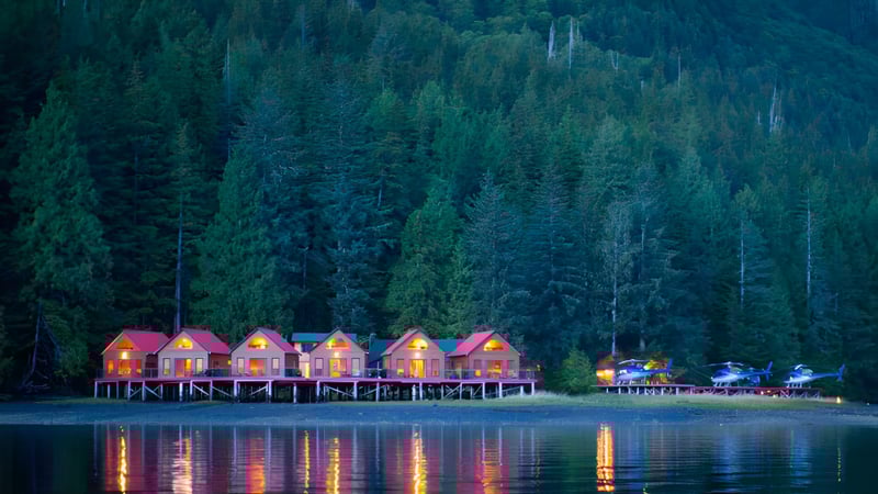 Ruhiger See mit farbigen Hütten und Wald im Hintergrund nahe der W.J. Mouat Secondary School.