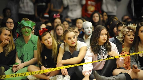 Eine Gruppe von Menschen in Kostümen sitzt hinter einer Polizeisperre bei einer Veranstaltung an der W.J. Mouat Secondary School.
