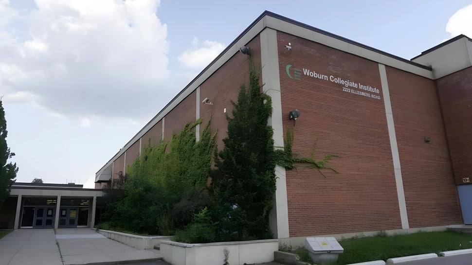 Das Gebäude des Woburn Collegiate Institute ist von grüner Vegetation umgeben und unter einem klaren Himmel zu sehen.