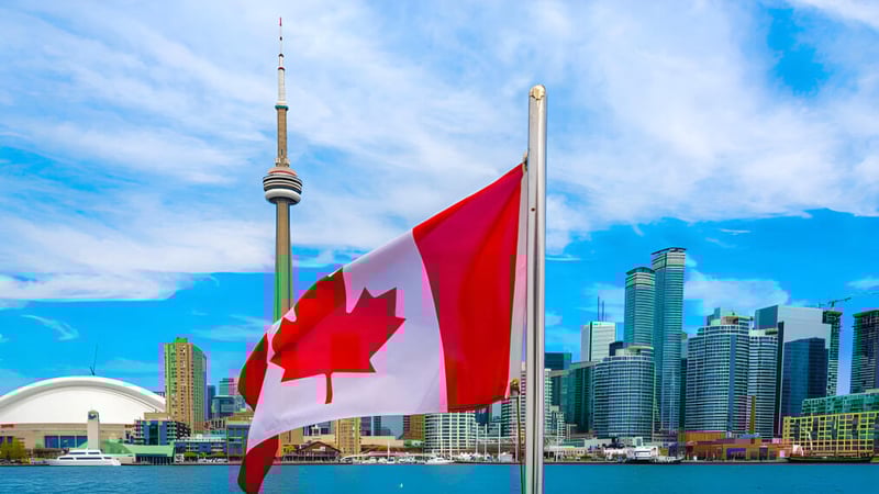 Eine große kanadische Flagge weht vor der Toronto Skyline mit dem CN Tower auf dem Campus des Woburn Collegiate Institute.