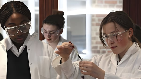 Drei Schülerinnen und Schüler der Woldingham School arbeiten konzentriert im Labor mit weißen Kitteln und Schutzbrillen.