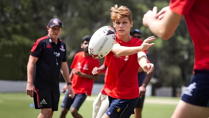 Ein junger Mann in rotem Trikot läuft mit einem Rugbyball über das Spielfeld auf dem Campus der Wollongong University.
