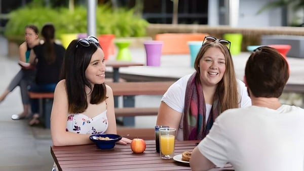 Schüler der Wollongong University genießen gemeinsam eine Mahlzeit im Freien vor einem bunten Hintergrund.