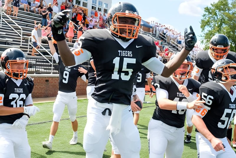Spieler der Woodberry Forest School in schwarzen und orangefarbenen Trikots feiern auf dem Spielfeld vor Zuschauern auf den Tribünen.