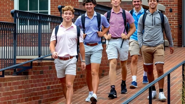 Eine Gruppe Schüler der Woodberry Forest School geht gemeinsam auf einem gepflasterten Weg vor einem Gebäude mit großen Fenstern.