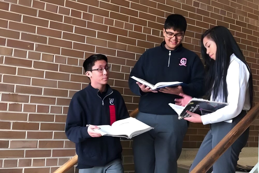 Drei Schülerinnen und Schüler des Woodbridge College stehen vor einer Backsteinwand und diskutieren gemeinsam.