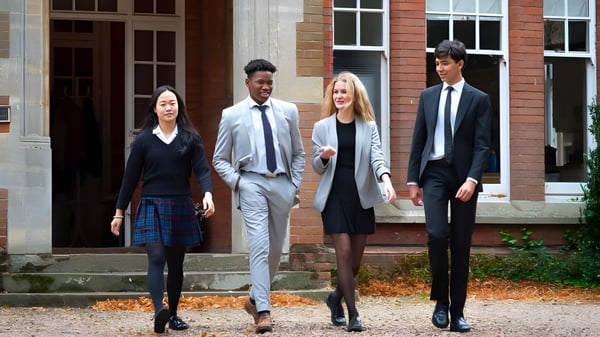Vier gut gekleidete Personen stehen auf den Stufen eines Backsteingebäudes auf dem Campus der Woodbridge School im Herbst.