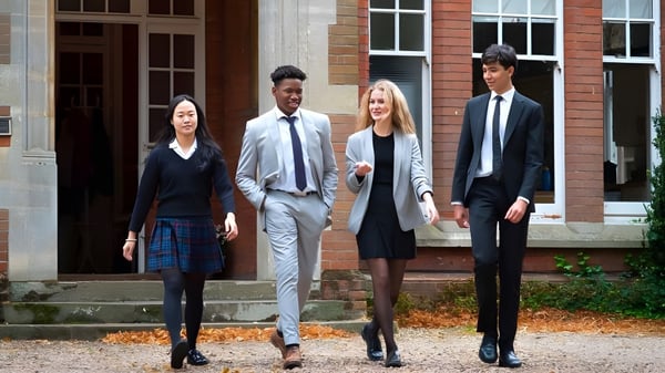 Vier gut gekleidete Personen stehen auf der Treppe eines Backsteingebäudes auf dem Campus der Woodbridge School im Herbst.