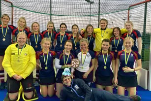 Eine Gruppe junger Sportlerinnen posiert vor einem Sportnetz auf dem Gelände der Woodbridge School.