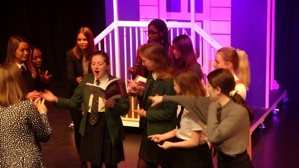 Eine Gruppe von Schülern der Woodbridge School steht auf einer Bühne mit bunter Beleuchtung im Theatersaal.