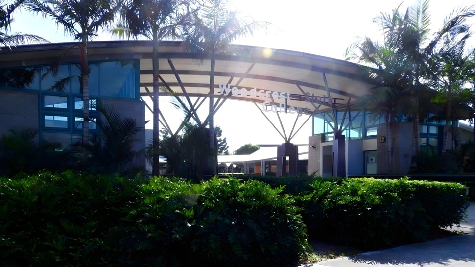 Das moderne Gebäude des Woodcrest State College zeichnet sich durch eine geschwungene Glas- und Stahlstruktur aus, umgeben von üppigem Grün.