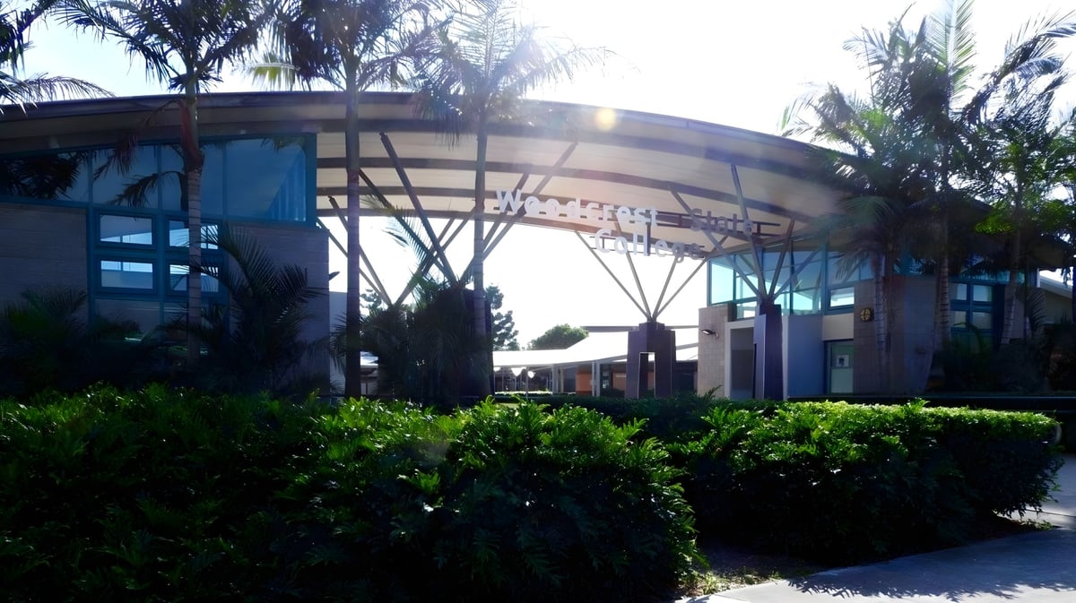 Das moderne Gebäude des Woodcrest State College zeichnet sich durch eine geschwungene Glas- und Stahlstruktur aus, umgeben von üppigem Grün.