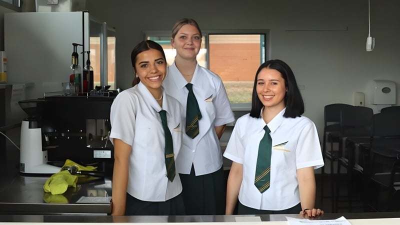 Drei Schülerinnen stehen gemeinsam in weißen Kitteln in einem Labor auf dem Campus des Woodcrest State College.