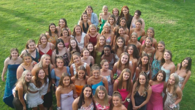 Eine Gruppe junger Frauen in bunten Badeanzügen und Kleidern steht auf einer Wiese auf dem Gelände der Woodford House.